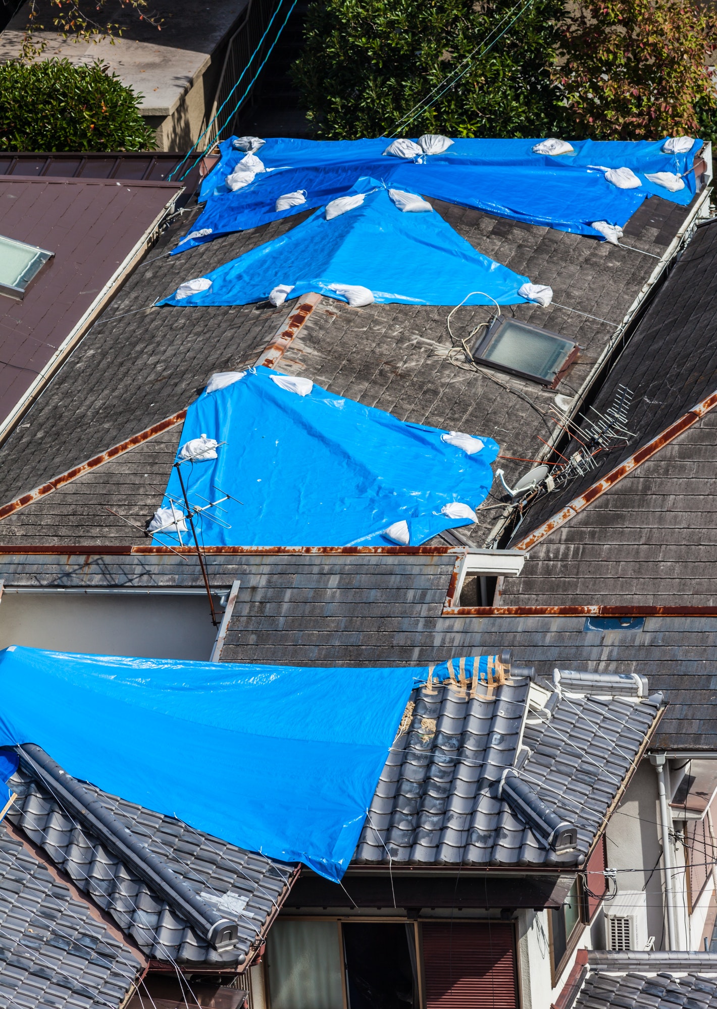 High angle view of houses hit by natural disaster, with damaged tiled roof covered with blue tarp